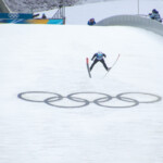 Ein Nordischer Kombinierer springt über die Olympischen Ringe.
