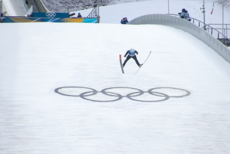 Ein Nordischer Kombinierer springt über die Olympischen Ringe.
