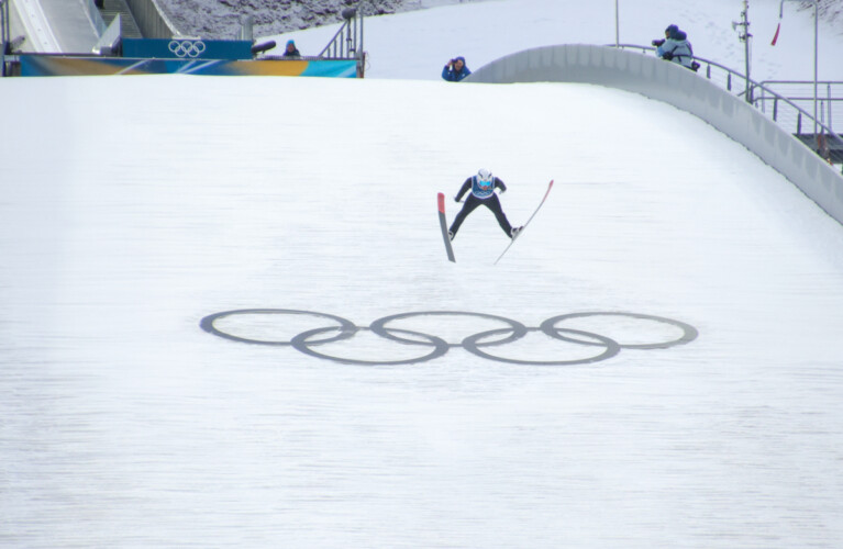 Ein Nordischer Kombinierer springt über die Olympischen Ringe.